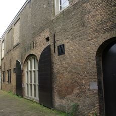 Groot pakhuis ter breedte van twaalf vensterassen, toegankelijk door twee getoogde poorten