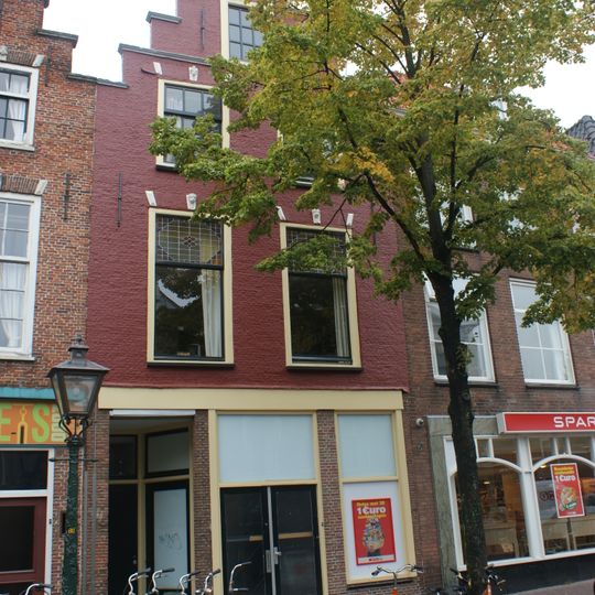 Pand met geverfde trapgevel met strekken en maskersluitingen, boven de vensters. Onderpui verbouwd, bovengevel in 1950 hersteld