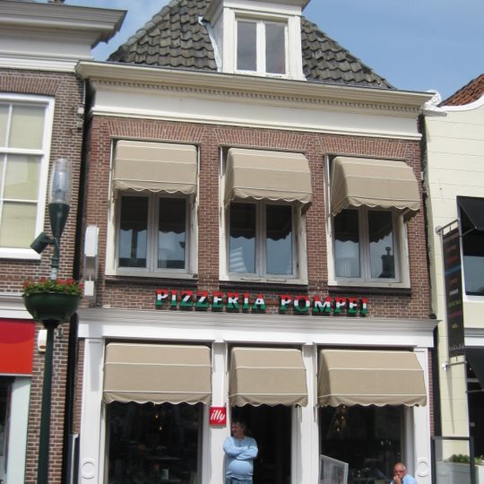 Pand onder zadeldak met achtertopgevel en gesneden kroonlijst in voorgevel waarvan pui in garage is gewijzigd