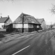 Bij het leegstaande boerderijtje Rheezerweg 95 langs de weg een schuurtje met wanden van stro en hout onder rieten schilddak