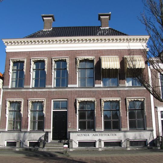 Drie traveeën breed pand met eenvoudige gevel met bloklijst aan kroonlijst, samen met nr. 49 onder U-vormig zadeldak