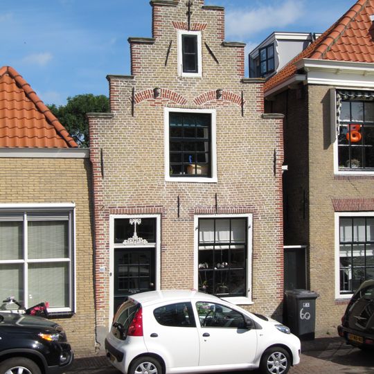 Huis met trapgevel met geprofileerde dekplaten en gewijzigde topafdekking. Ontlastingsbogen van vroegere vensters. Topanker