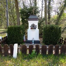 Beschreibung weiss verputzter 2 stufiger Bildstock mit Ädikula darin Marienfigur. Bekrönt von einem Metallkreuz