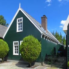 Houten huis met gerabatte wanden met zolderverdieping onder zadeldak met puntgevel met makelaar