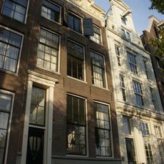 Pand met gevel onder rijk gebeeldhouwde stenen, in het midden verhoogde lijst met siervaas