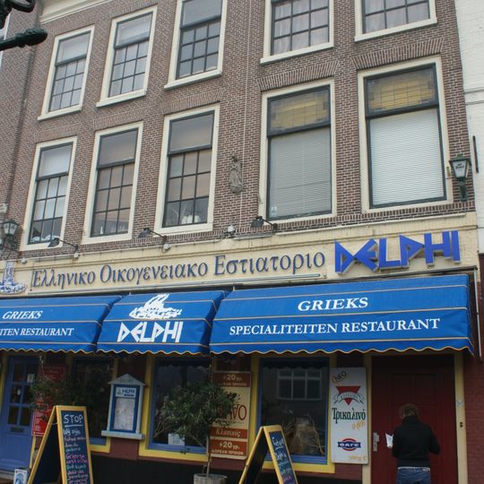 Pand met bakstenen gevel met rechte kroonlijst. Oorspronkelijk twee gevels, onderpui in 1938 vernieuwd. Terracotta Heilige beeld en d.g.l. moderne toevoegingen