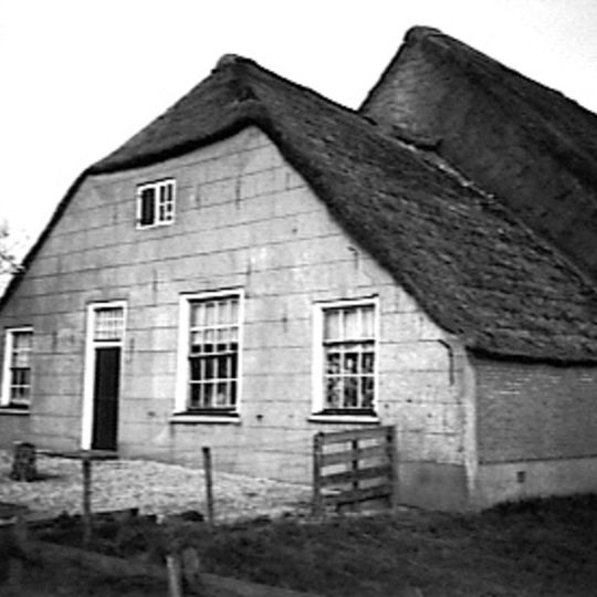 Boerderij met karakteristieke hoofdvormen: lager woonhuis onder rieten wolfdak en met gepleisterde gevel, waarin vensters met twintig, twaalf- en zesruitsschuiframen