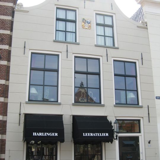 Hoog pand onder zadeldak tegen klokgevel met aanzetkrullen en halfronde bekroning met wapenschild