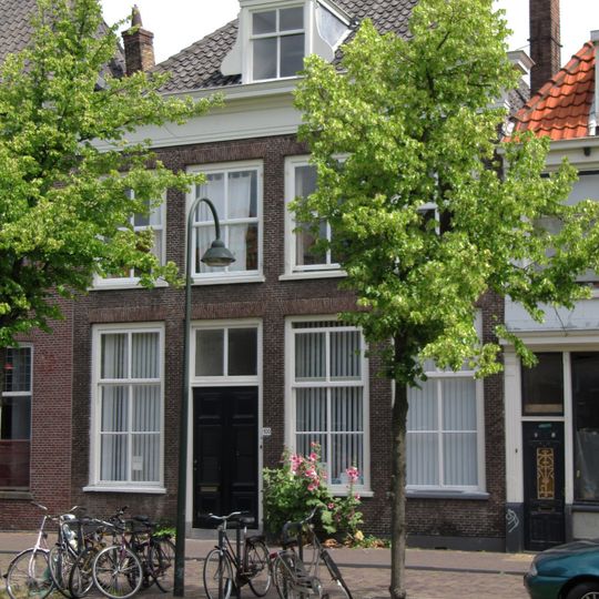 Pand et verdieping en dwars schilddak, waarin dakkapel met vleugelstukken. Vensters met zes- en vierruitsramen. Houten kroonlijst