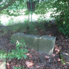 Povalený podstavec s ulomeným kovovým křížem pod lípou v lukách u Lipové