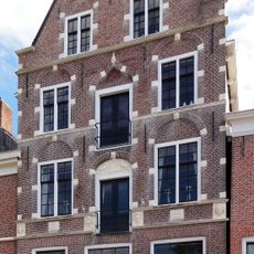 Vernieuwd hoog pand onder zadeldak tussen puntgevels, waarvan de voorste rijk bewerkt