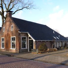 Woning met zesruitsvensters en kleine topvensters onder breed zadeldak met topschoorsteen met bord en stal in het verlengde van de woning