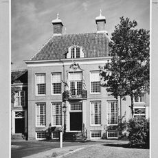 Pand bestaande uit vooruitspringende lijstgevel, op de hoeken van het dak, grote schoorstenen, versierde régence ingangspartij, fraai gesmeed balkonhek