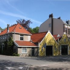 Langgerekte houten schuur onder zadeldak en eenvoudige geverfde puntgevel. Met inrijpoort