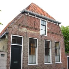 Woonhuis met verdieping. Topgevel ingezwenkt en afgeknot. Pui gewijzigd in andere steen; oorspronkelijk mooie rode steen