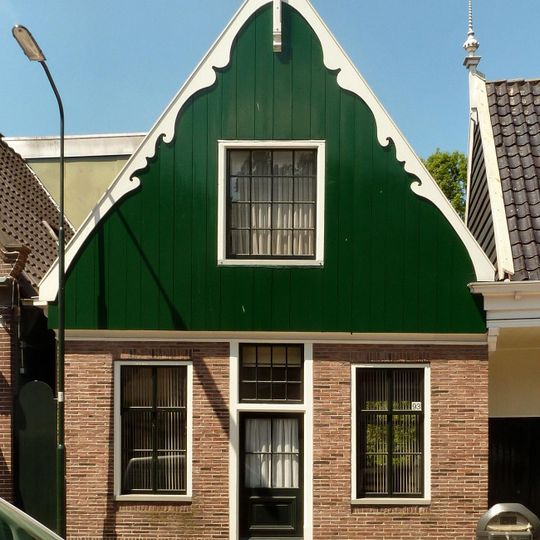 Grotendeels houten huis, waarvan het zadeldak wordt afgesloten door een houten topgevel met uitgeschulpte windveren. Bakstenen pui