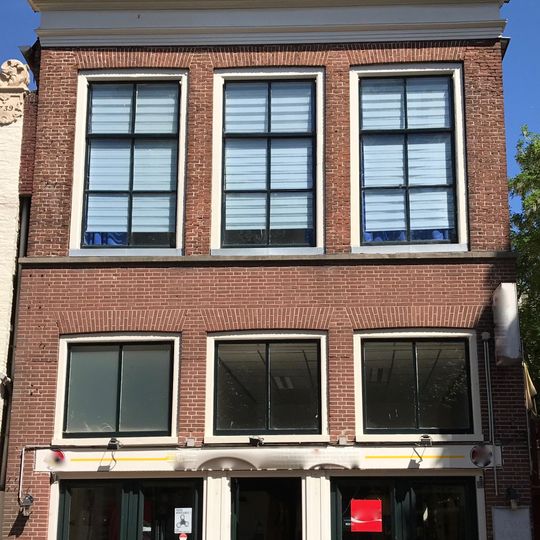 Pand onder zadeldak met topschoorsteen en gevel met rechte kroonlijst boven moderne pui