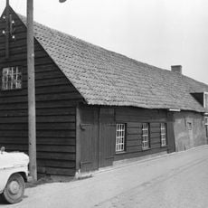 Langgerekte boerderij onder pannendak en met een puntgeveltje boven het woongedeelte. Links de schuur met gepotdekselde houten delen