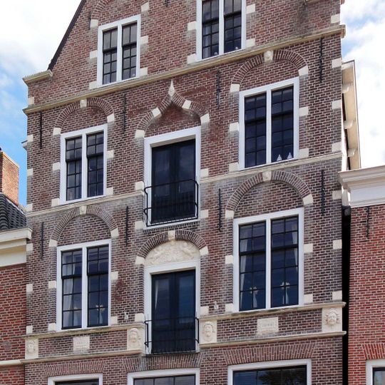 Vernieuwd hoog pand onder zadeldak tussen puntgevels, waarvan de voorste rijk bewerkt