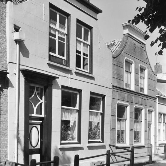 Huis met gepleisterde lijstgevel met ingezwenkte top. Voordeur en vensteromlijstingen met afgeschuinde hoeken. Voordeur met na-empire velden.