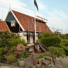 Hoekpand aan voorzijde van de gedempte havenkom met goed gedetailleerd houten voorschot. Bij dit pand behoort houten schuur met tuinpoortje erachter
