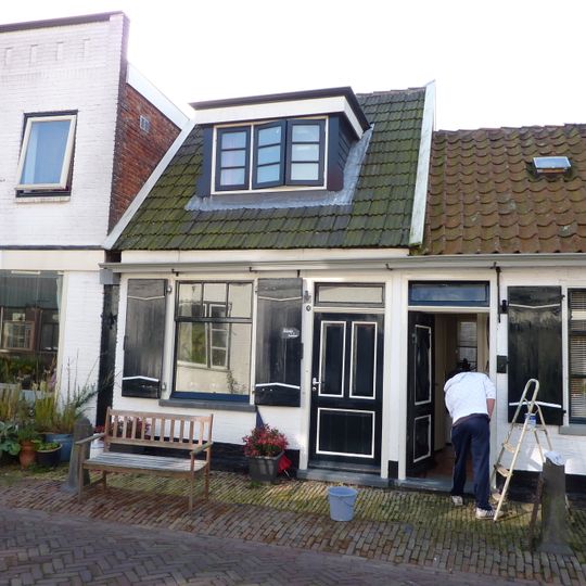 Klein huisje onder een dwarsdak met de nummers 8 en 10. Aardige details aan de vensters, luiken en achterschot