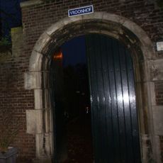 Boogpoort in gotische trant met natuurstenen omlijstingen, toegang gevend tot de school