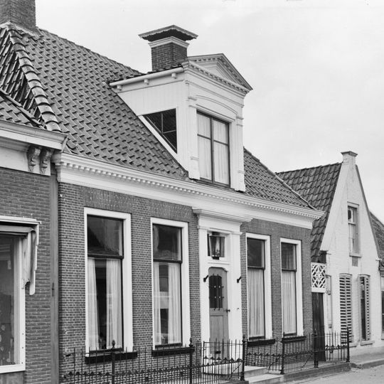 Landelijk huis met omlijste ingang onder schilddak met versierde dakkapel en twee hoekschoorstenen met borden