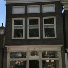 Hoog pand met vernieuwde voorgevel met lage vensters op zolderverdieping en kroonlijst onder zadeldak met voorschild waarboven topschoorsteen met bord