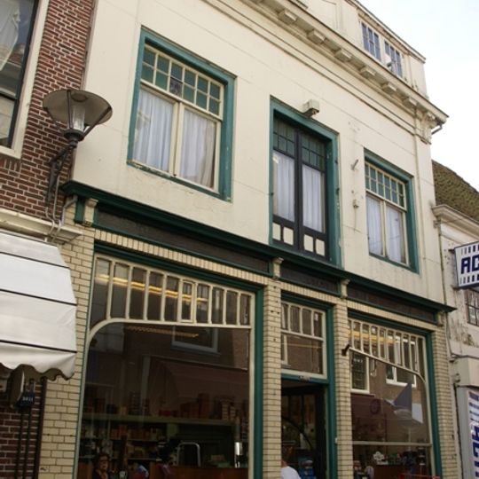 Pand met boven sterk gewijzigde en gepleisterde gevel met laat 18e-eeuwse attiekverdieping met vrij gebeeldhouwd wapenschild voor dwarskap