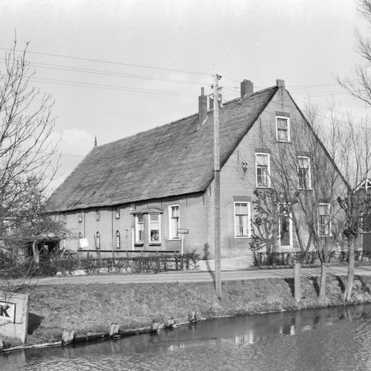 Grote boerderij onder hoog, rieten zadeldak met aan de voorzijde een IJsselstenen puntgevel met vlechtingen en rode strekken boven de vensters