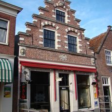 Huis met houten puntgevel boven een pui met een gebogen hoekvenster en aan weerszijden van de ingang pilasters