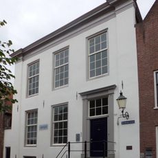 Huis met gepleisterde forse lijstgevel aan de zijkanten iets naar voren springend. 19e-eeuws karakter; echter oudere opzet aanwezig